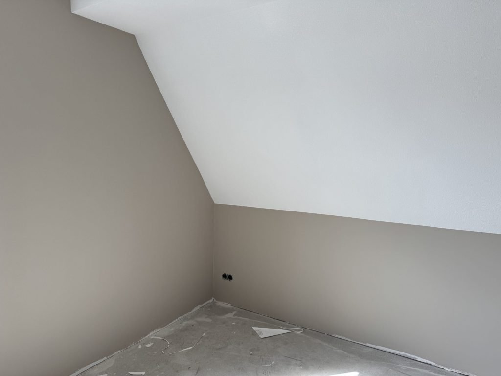 Zolderkamer met schuin dak en egaal afgewerkte beige wanden op een nog kale betonvloer