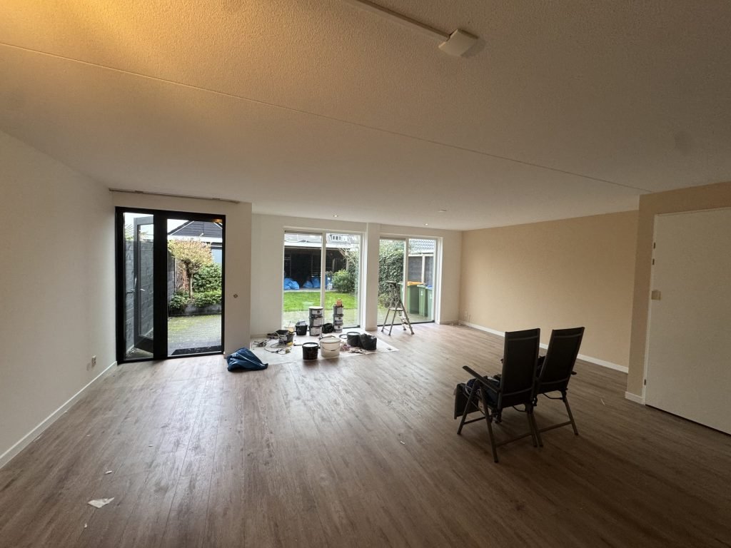 Ruime woonkamer met licht afgewerkte wanden, houten vloer en tuindeuren tijdens de afwerking